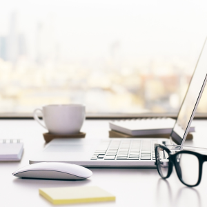 image d'un bureau recouvert d'un ordinateur portable, d'une tasse à thé, d'une souris, de blocs-notes, de lunettes noires et d'un bloc-notes jaune.