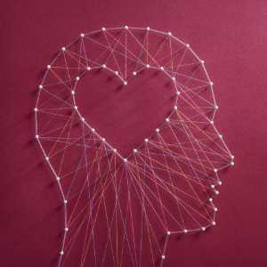 Profile of a head with a heart inside, made with strings and pins on a red background.