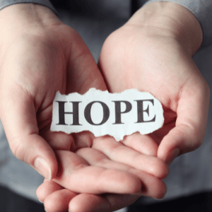 Hands holding a piece of paper between them that says the word hope